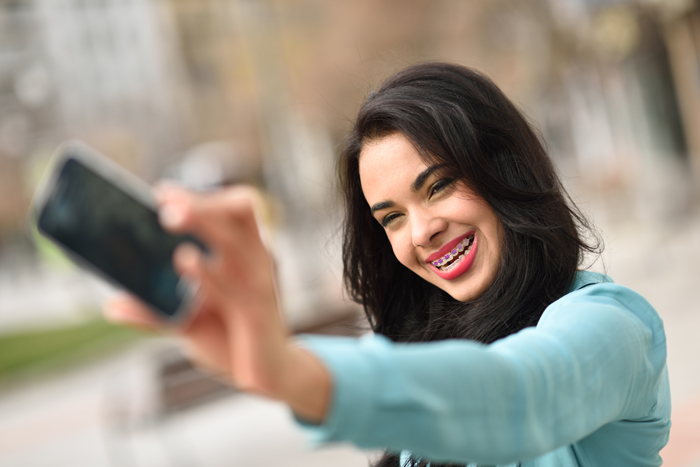 Portrait of a beautiful young woman, using braces, selfie in the street with a smartphone